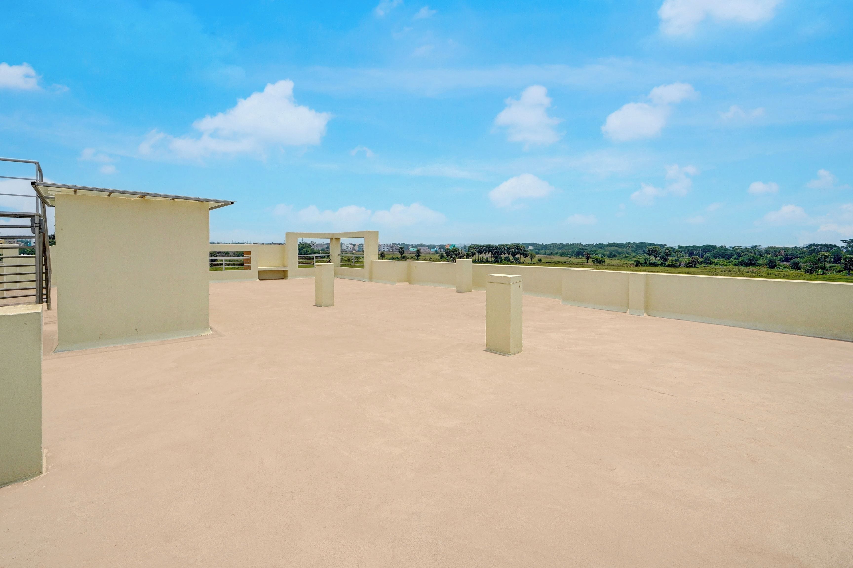 A rooftop terrace with a clear sky, concrete pillars, and a view of distant buildings and greenery.