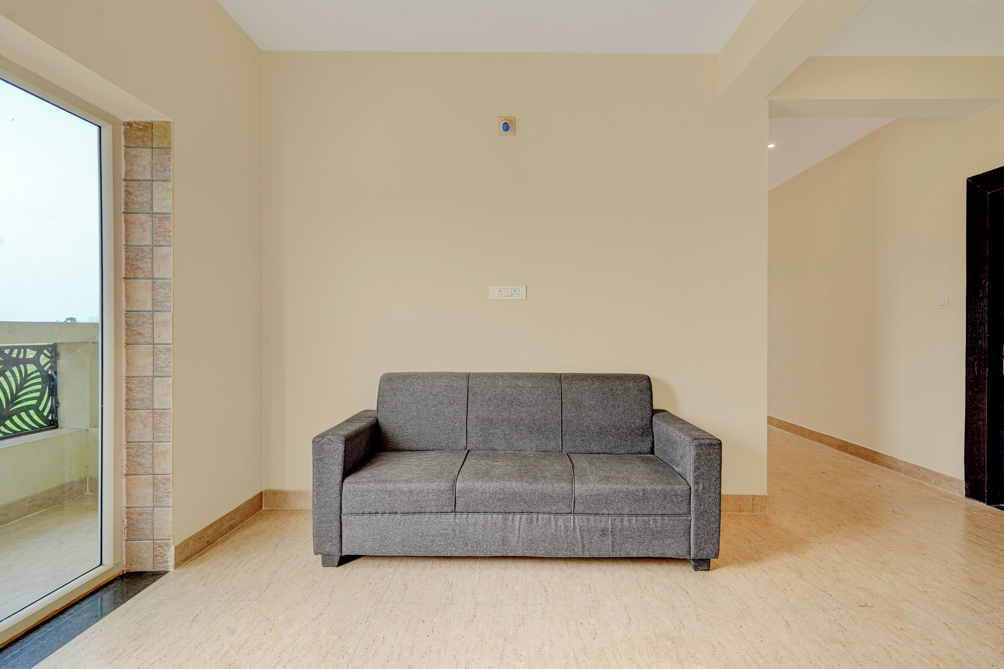 Una sala de estar en tonos neutros, con un sofá gris, piso de baldosas y una puerta que da a otra habitación.