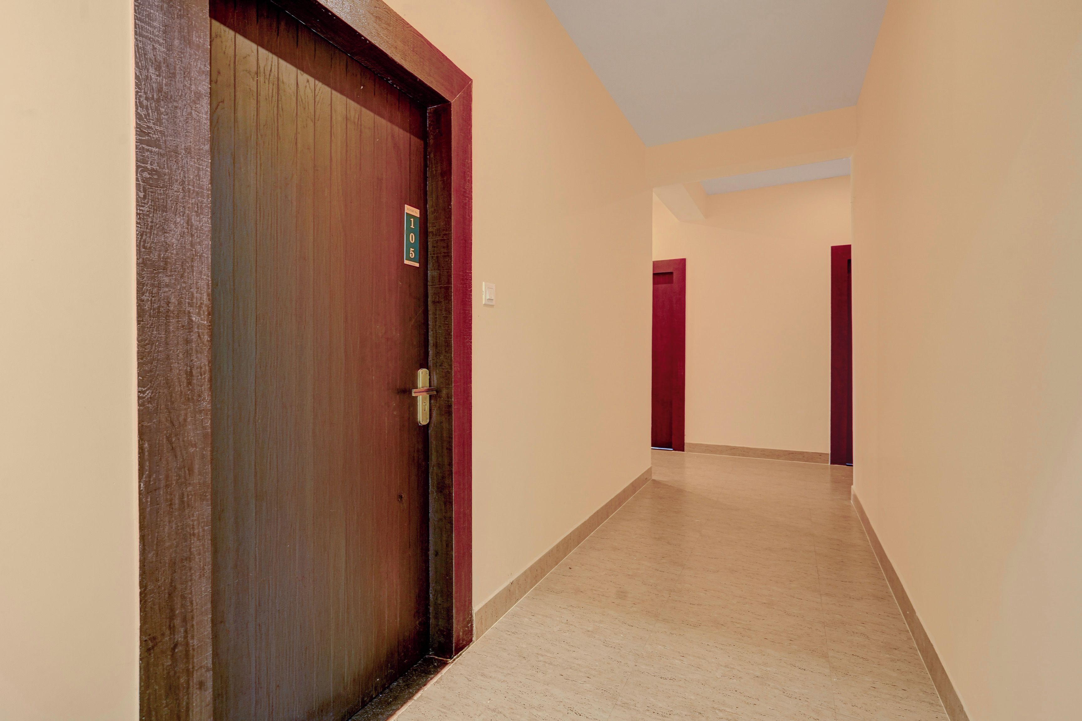 A corridor with a wooden door, beige walls, and a tiled floor.