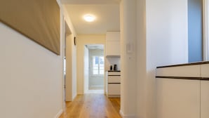 A corridor with wooden flooring leading to a kitchen area with white cabinets and a window. - The Cloud  Apartment (Zurigo)
