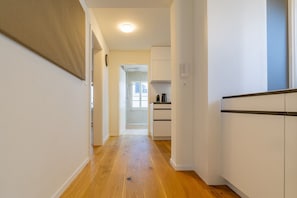 Ein Korridor mit Holzdielen führt zu einer Küchenzeile mit weißen Schränken und einem Fenster.
