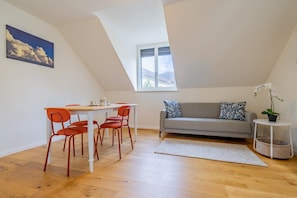 Ein Zimmer mit Esstisch und Stühlen, einer Couch, einem Fenster und einer Pflanze.