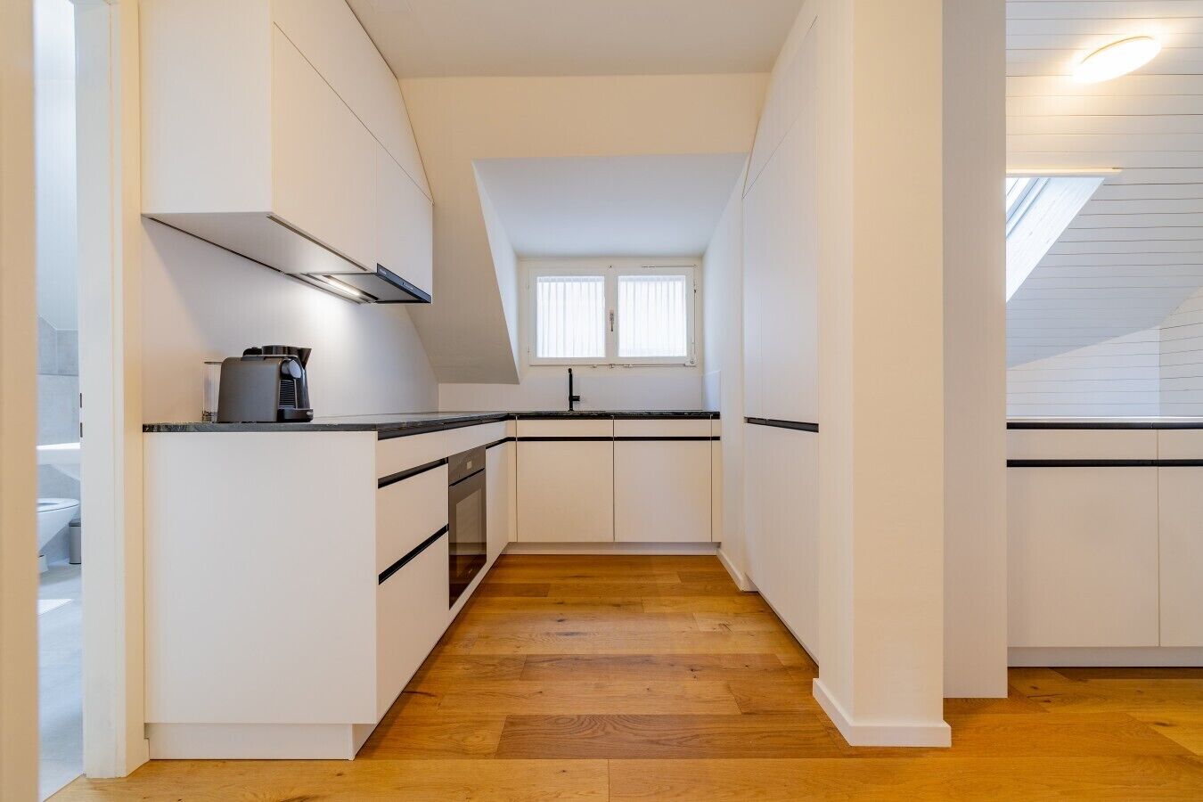 Eine moderne Küche mit weißen Schränken, einer schwarzen Arbeitsplatte und einem Fenster für natürliches Licht.