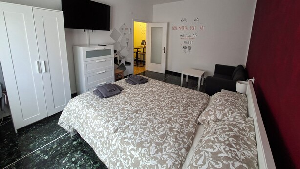 A hotel room with a bed, a TV, a wardrobe, a desk, and a red accent wall. - On vacation but with all the comforts of home, just a 5-minute walk from the beach (Recco)