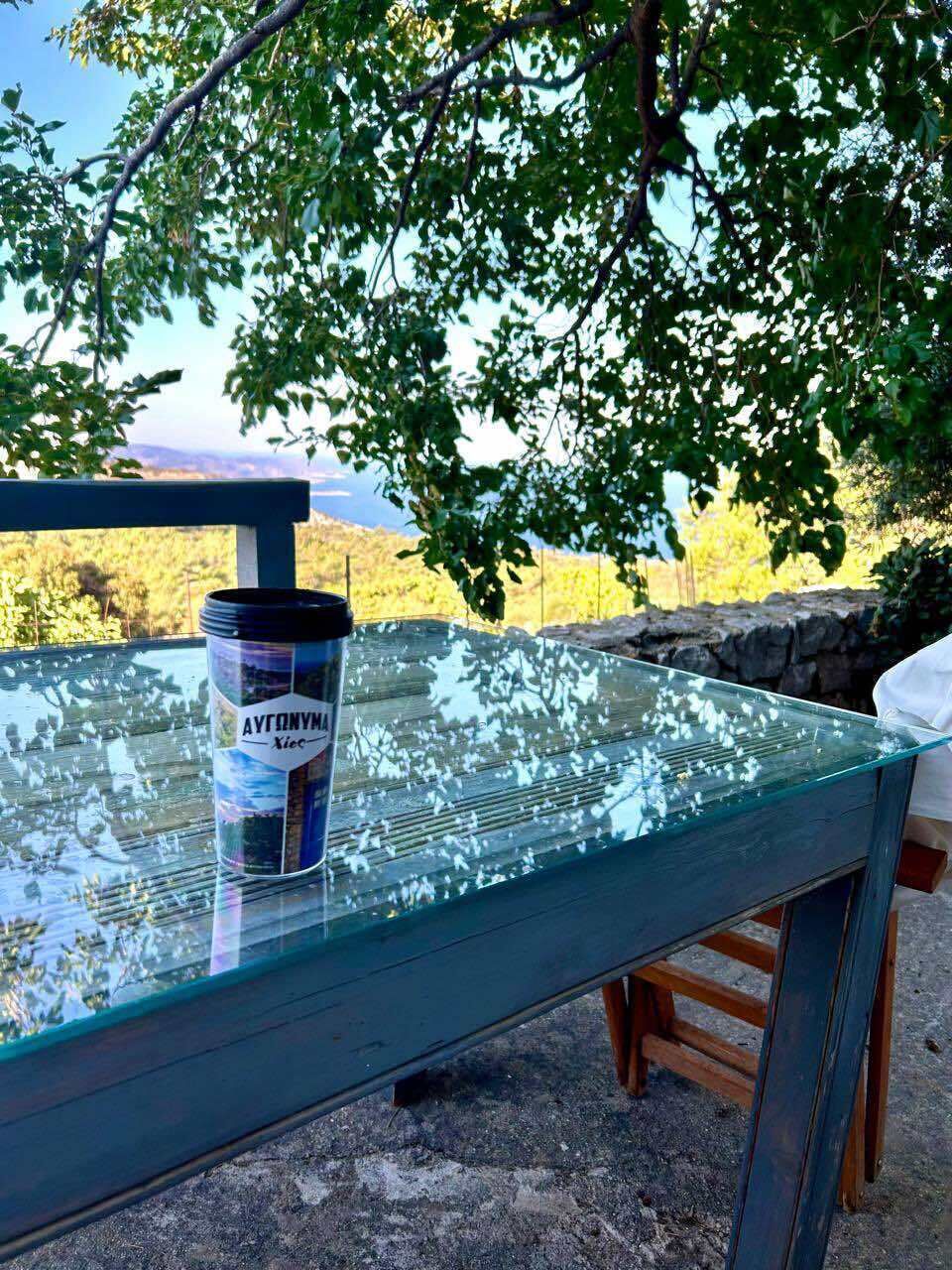 A glass table with a cup on it, set outdoors with a view of trees and a distant landscape.