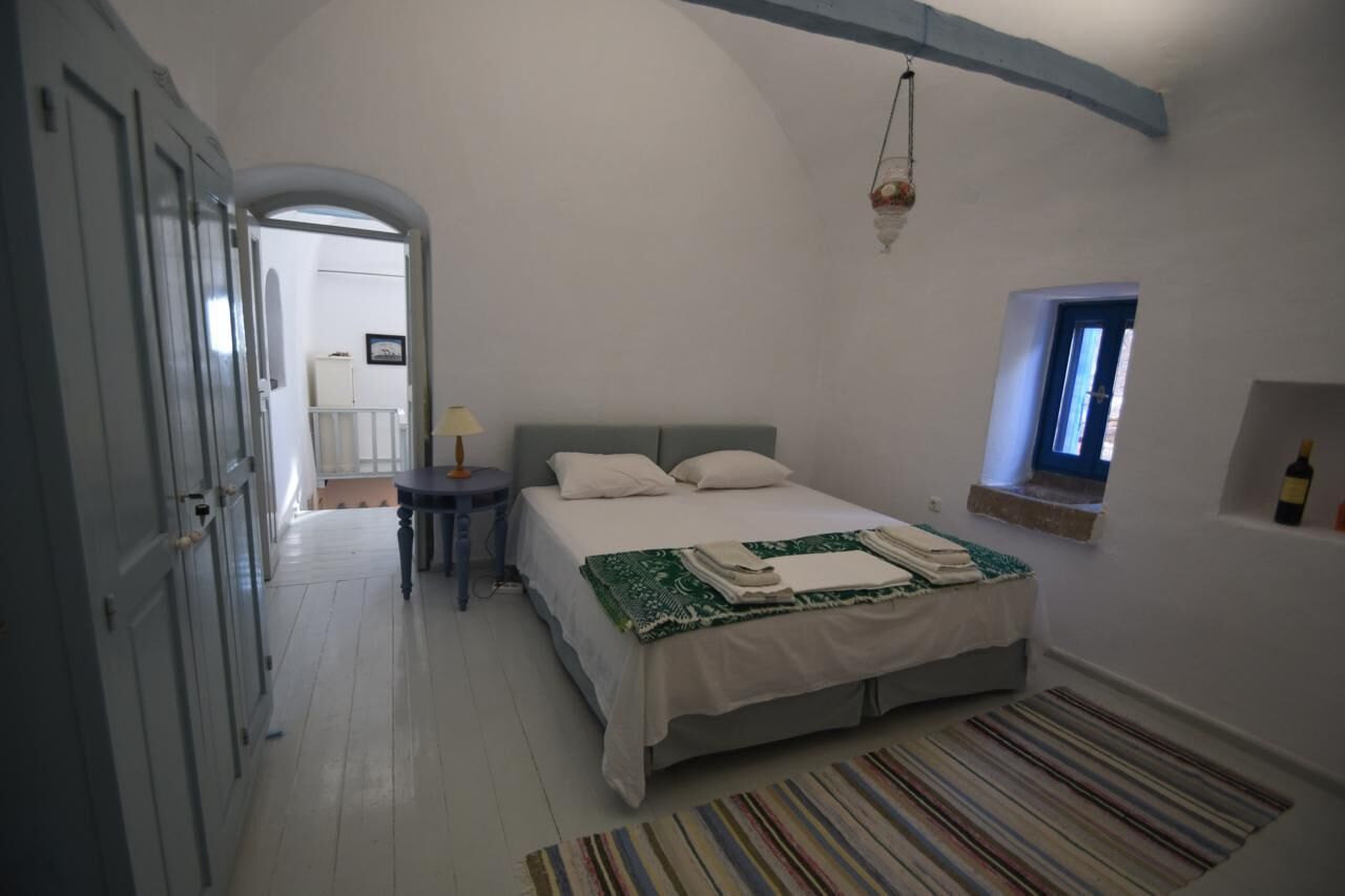 A bedroom with a bed, a small table, a lamp, a window, and a door.