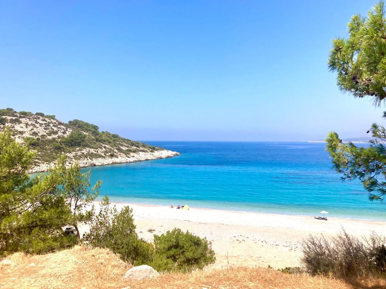 Paisagem costeira com praia, mar azul cristalino e vegetação esparsa.