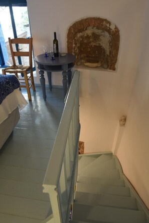 A staircase with a handrail, a wooden chair, a small round table with a bottle and glasses, and a wall-mounted object. - Avgonima Joy Medvial Suite (Chios)