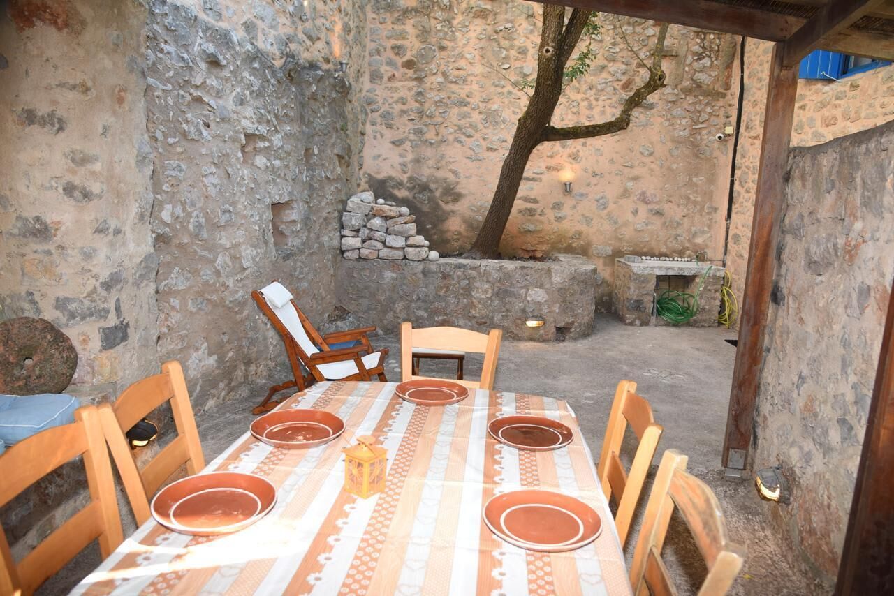 An outdoor dining area with a stone wall, wooden chairs, a table set with plates, and a lantern.