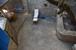 An outdoor patio area with stone walls, a wooden table with chairs, a lounge chair, and a small blue stool. - Avgonima Joy Medvial Suite (Chios)