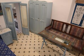 A room with a blue wardrobe, a glass-top table, patterned sofa, and a tiled floor. - Avgonima Joy Medvial Suite (Chios)
