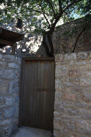 A stone wall with a wooden door, a tree, and a stone structure above the door. - Avgonima Joy Medvial Suite (Chios)