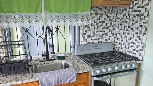 A kitchen with wooden cabinets, a gas stove, a sink, and a patterned backsplash. - Wonderful 1-bedroom house with AC in charming Marigot (Marigot)