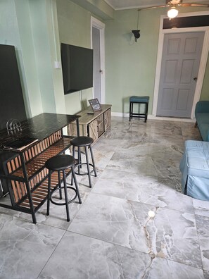A room with a bar area, a television mounted on the wall, a door, and a seating area with a bench. - Wonderful 1-bedroom house with AC in charming Marigot (Marigot)