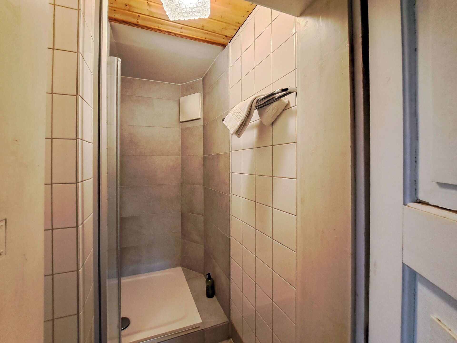 Um banheiro pequeno com revestimento de azulejos, teto de madeira e uma toalha branca pendurada na parede.
