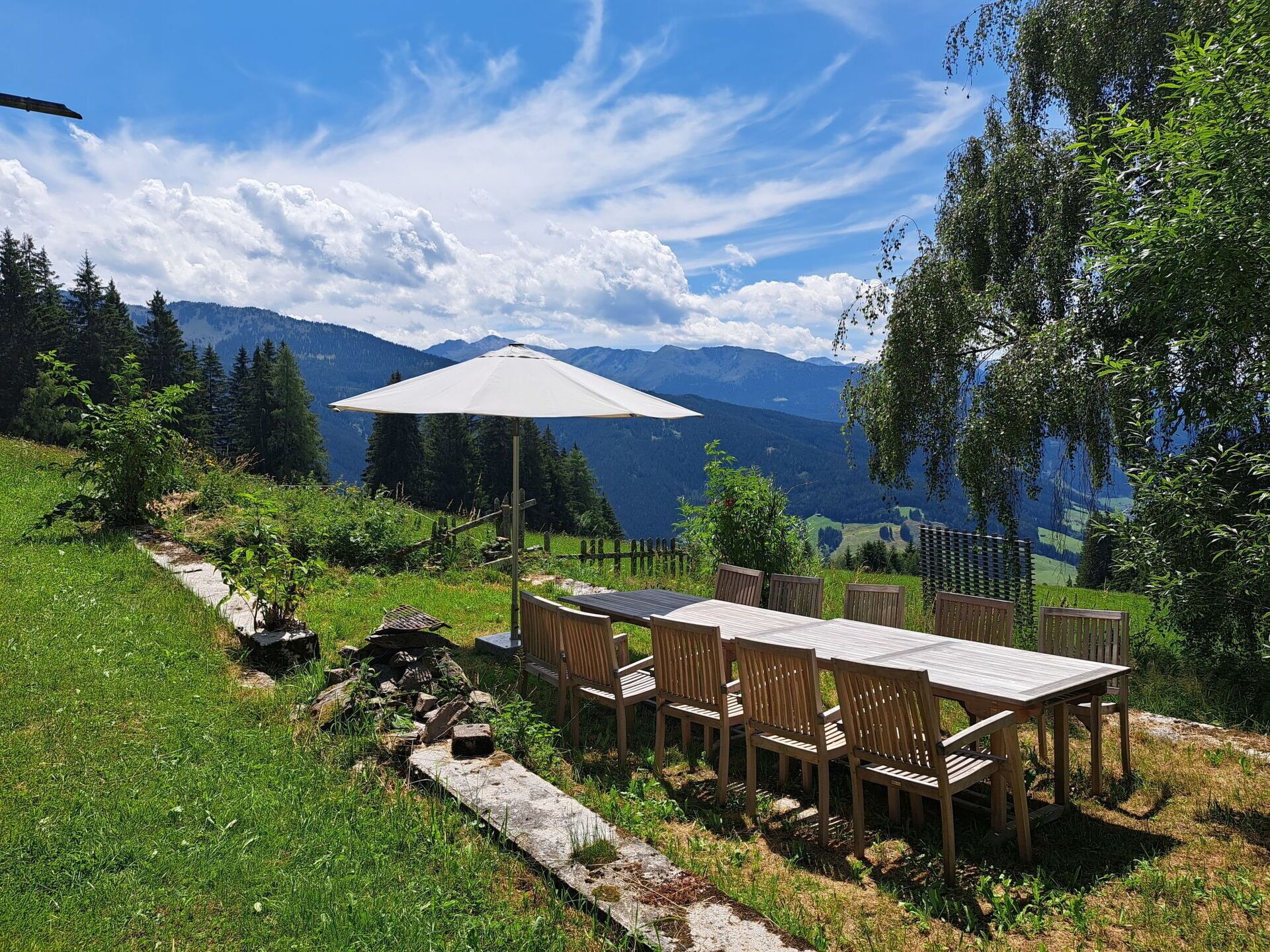 Een terras met een tafel en stoelen, omgeven door een grasrijk landschap en uitzicht op bergen.