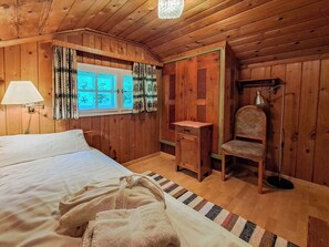 A wooden room with a bed, a desk, a chair, a lamp, and a window with curtains.