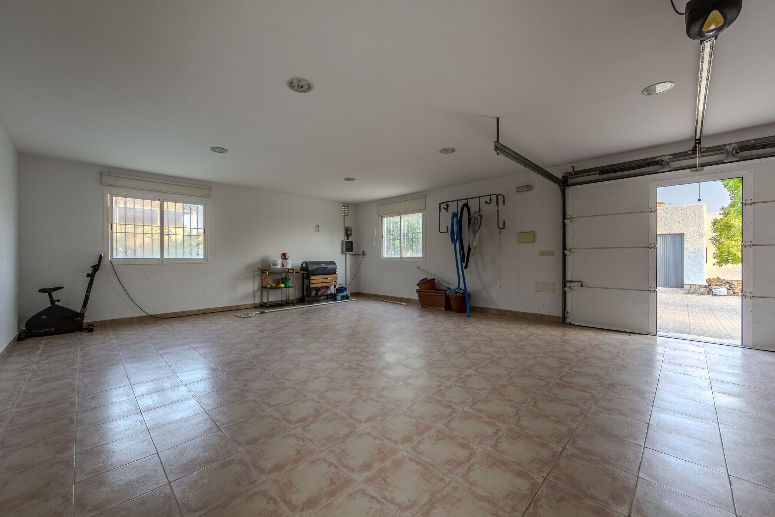 A spacious room with a tiled floor, a ceiling fan, a window with bars, and a door leading outside.