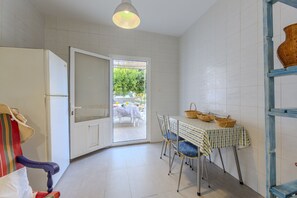 Eine Küche mit Esstisch, Stühlen, einem Kühlschrank und einer hängenden Körbchen.