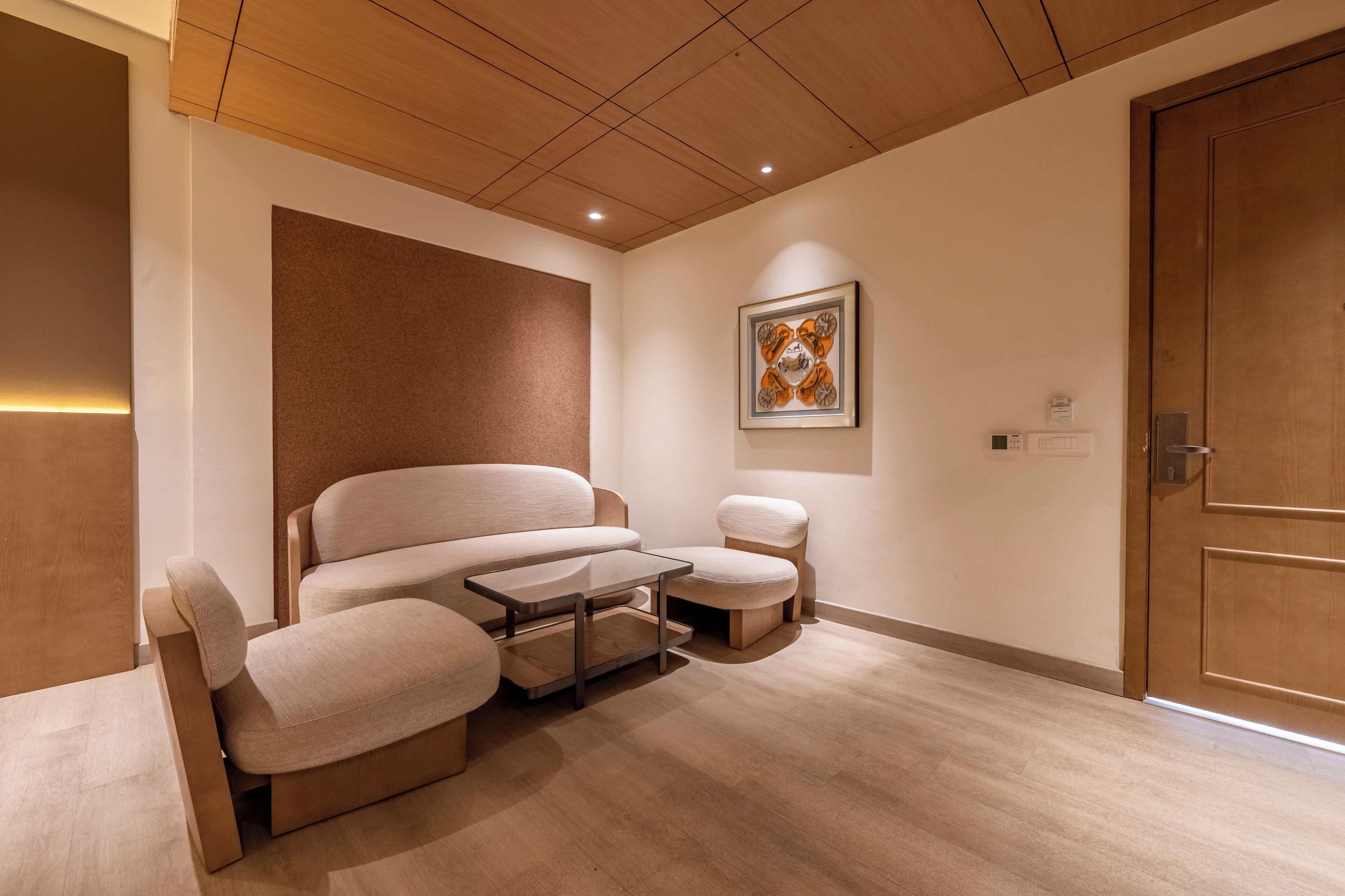 A modern room with a sofa, a small table, and a chair. There is a wooden door and a framed picture on the wall.
