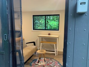 A room with a window, a small wooden desk, a chair, and a patterned rug.