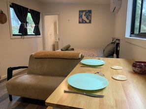 A cozy room with a sofa, a dining table with plates and cutlery, a decorative bowl, and a painting on the wall.