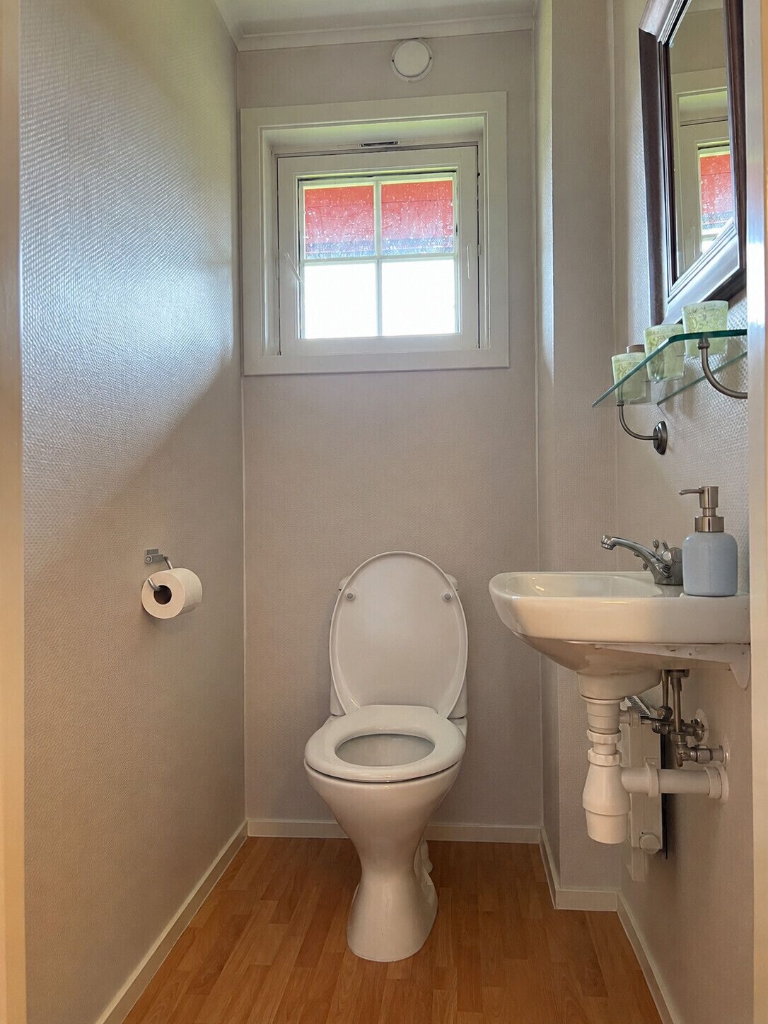 A small bathroom with a toilet, a sink, and a window above the toilet.
