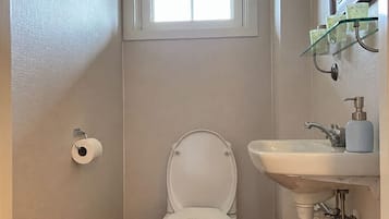 A small bathroom with a toilet, a sink, and a window above the toilet.