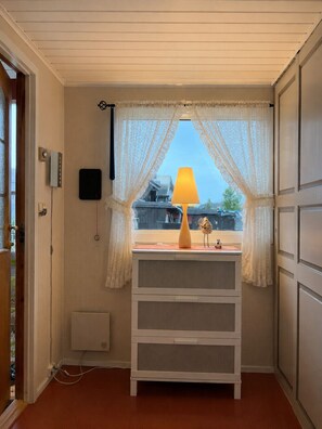 Una habitación con ventana, una lámpara, una mesita pequeña y un armario blanco.