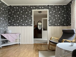 Una habitación con piso de madera, una silla, una mesa pequeña cubierta con un mantel rosa y una pared con estampado floral.