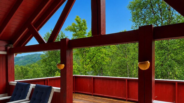 A covered deck with red railings, two blue cushioned chairs, and a view of a forested mountain. - Spacious Home in Sudndalen at the Foot of Hallingskarvet (Hol)