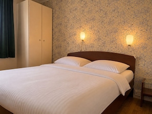 Una habitación de hotel con una cama, dos lámparas de pared, un armario y un papel tapiz estampado.