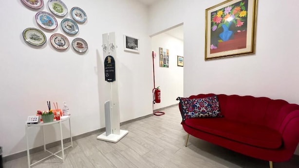 Una habitación con un sofá rojo, una mesa blanca con una pequeña planta y una pared decorada con platos y un cuadro enmarcado.