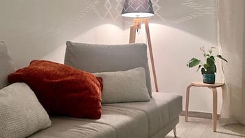 Una sala de estar moderna con un sofá, cojines, una lámpara de pie y una mesita con una planta.