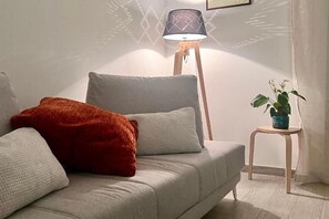 A modern living room with a sofa, pillows, a floor lamp, and a small table with a plant.