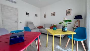 Una sala de estar con un sofá, una mesa roja, una mesa amarilla y una silla azul.