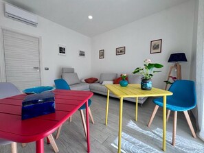 A living room with a sofa, a red table, a yellow table, and a blue chair.