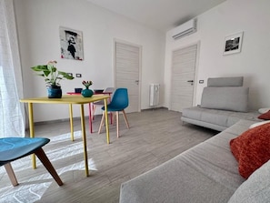 A modern living room with a sofa, a dining table with chairs, and a potted plant.