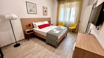 Una habitación de hotel con cama, mesita de noche, lámpara y televisión.
