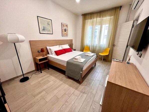 A hotel room with a bed, bedside table, lamp, and a TV.
