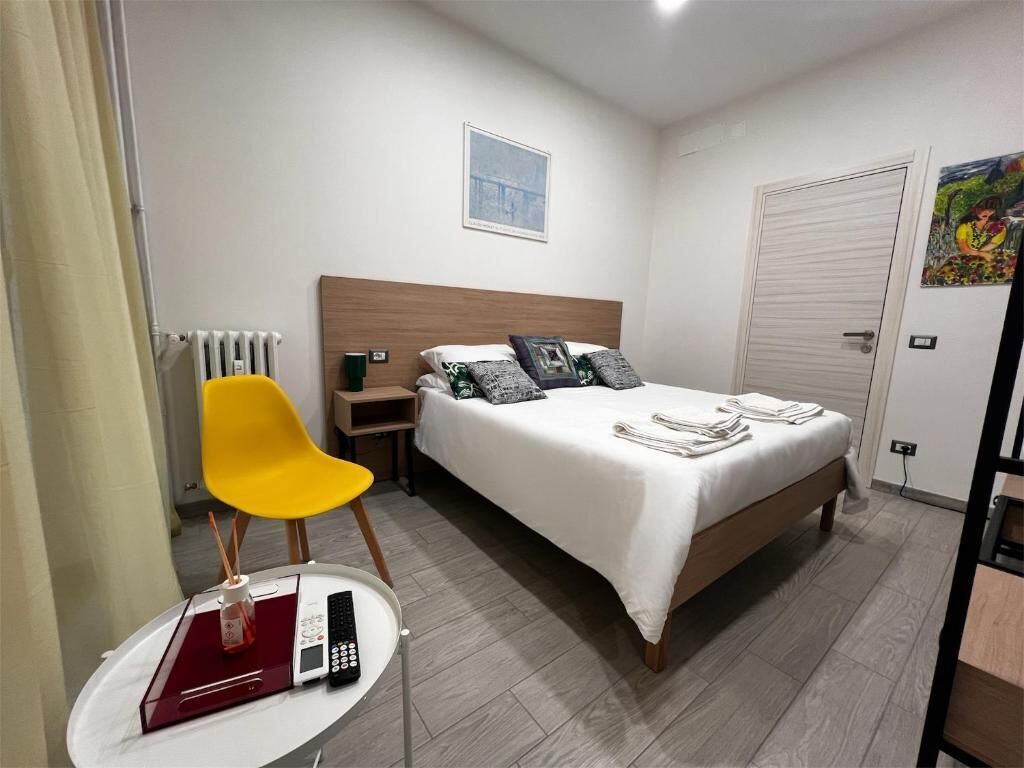A bedroom with a bed, a bedside table with a remote control, a chair, and a radiator.