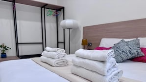 Una cama bien hecha con toallas blancas dobladas y una mesita de noche con una lámpara y una pequeña planta en maceta.