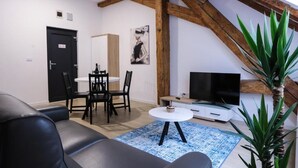 Ett modernt vardagsrum med en svart lädersoffa, ett matbord med stolar, en platt-TV och en blå, mönstrad matta.