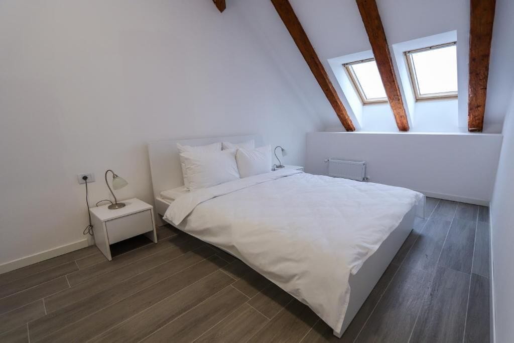 A bedroom with a bed, bedside table, lamp, and skylight windows.