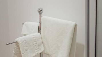 Ein Badezimmer mit Handtuchhalter, der zwei weiße Handtücher trägt, Holzboden und einer Duschkabine aus Glas.