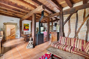 Ein rustikales Interieur mit freiliegenden Holzbalken, einem Kamin aus Stein, einer Buddha-Statue und einem gemusterten Sofa.