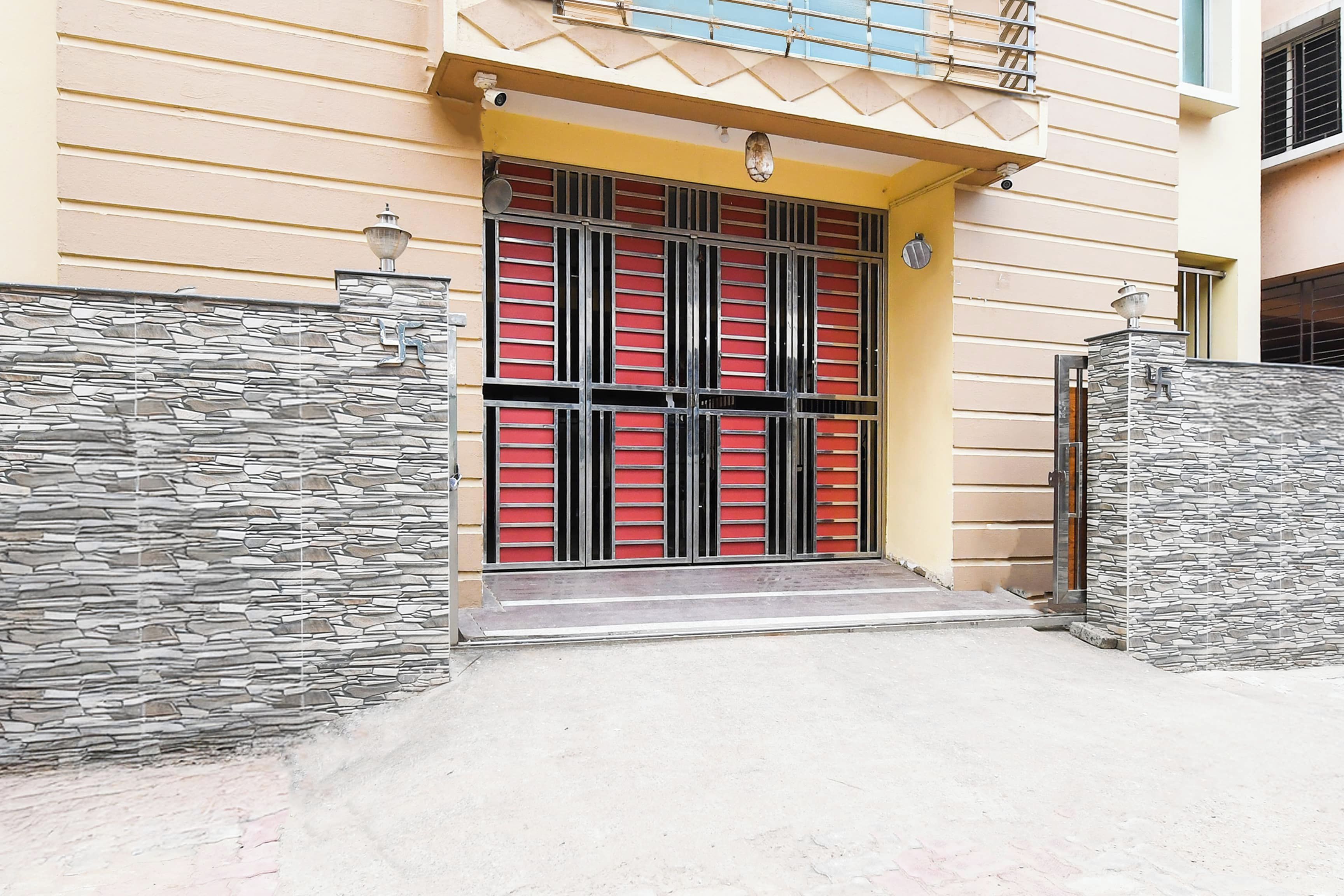 A building with a yellow facade, a gated entrance with red and black metal bars, and a stone-textured wall on one side.