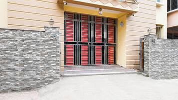 A building with a yellow facade, a gated entrance with red and black metal bars, and a stone-textured wall on one side.