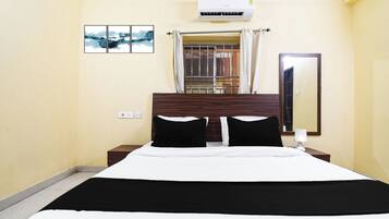 A hotel room with a bed, a nightstand, a mirror, an air conditioning unit, and a window with curtains.