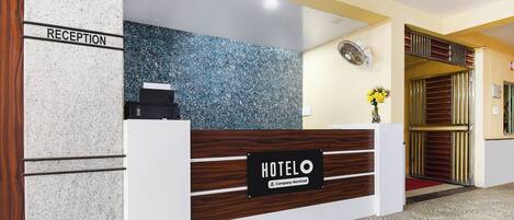 Una reception hotel con un cartello 'HOTELO', un'area di accoglienza e una ventola a parete.